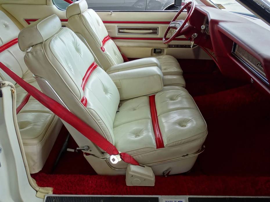 Assento dianteiro de um Lincoln Mark IV de 1975 com detalhes vermelhos em assentos de couro branco e cintos de segurança vermelhos brilhantes
