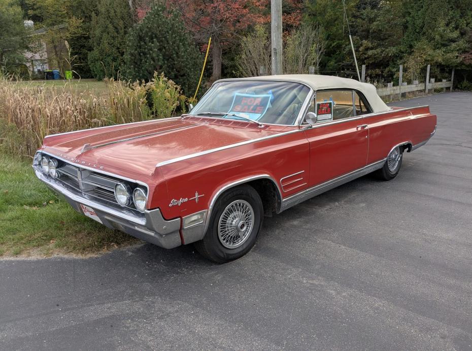 1964 Oldsmobile Starfire Convertible parked on the road with a FOR SALE sign.